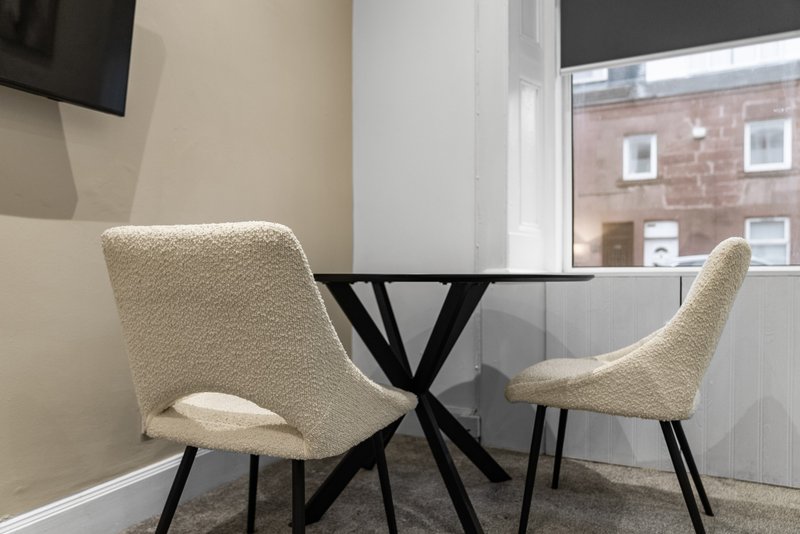 Modern dining area with two cream upholstered chairs and glass table, window with street view