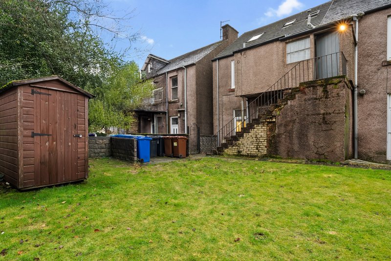 Rear garden with lawn, stone outbuildings, wheelie bins and wooden shed