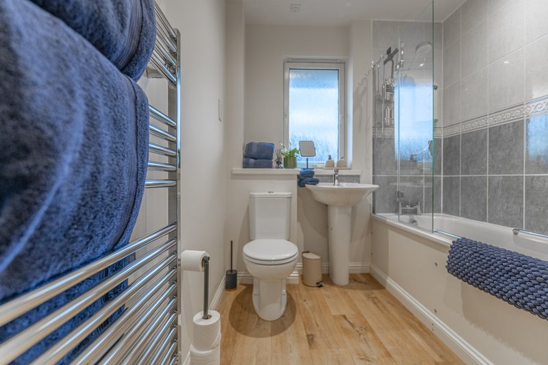 Modern bathroom with toilet, sink, shower enclosure, heated towel rack and wood flooring