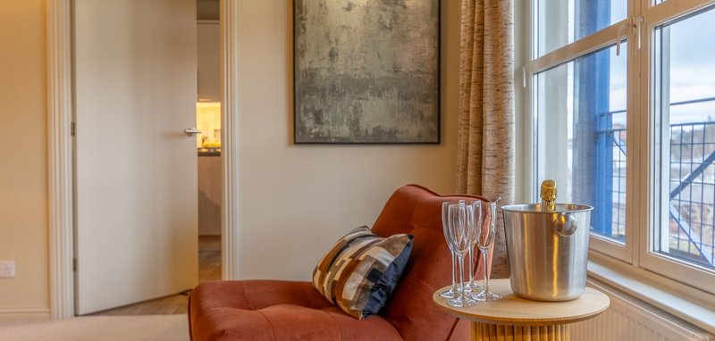 Modern apartment corner with rust-colored armchair, side table, and large windows with city views