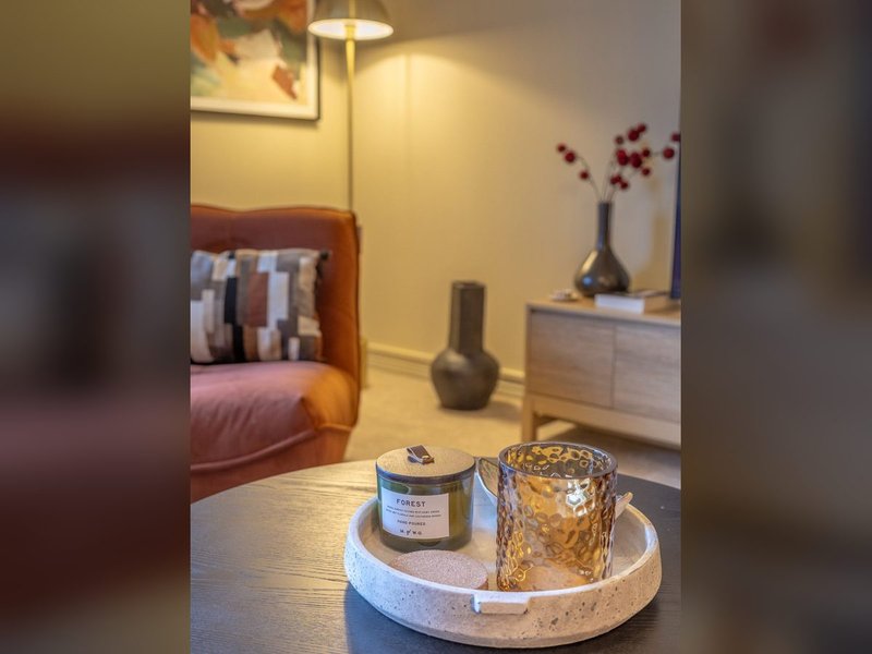 Modern bedroom with orange accent chair, wooden table with candle and decorative items, floor lamp