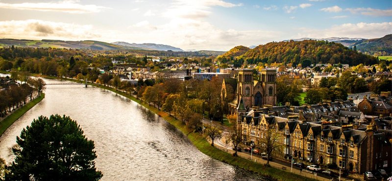 River valley landscape with historic stone buildings, tree-lined banks and distant hills