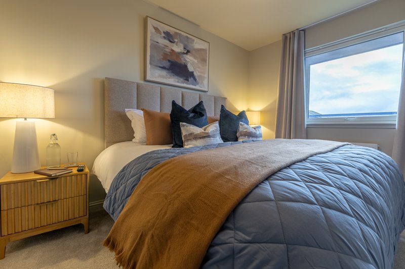 Modern bedroom with double bed, upholstered headboard, decorative pillows and bedside lamp