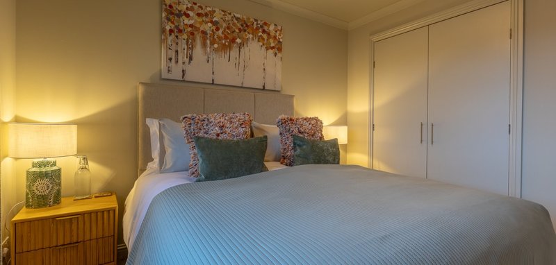 Bedroom with double bed, decorative pillows, bedside lamps, and wall art
