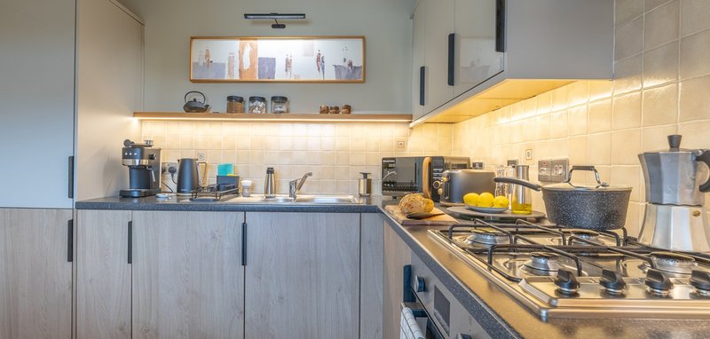 Modern kitchen with gas hob, fitted cabinets, stainless steel appliances and warm lighting