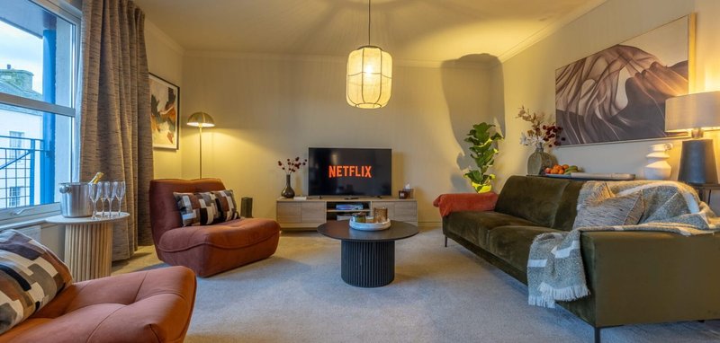 Spacious living room with comfortable seating, TV, pendant lighting, plants and artwork