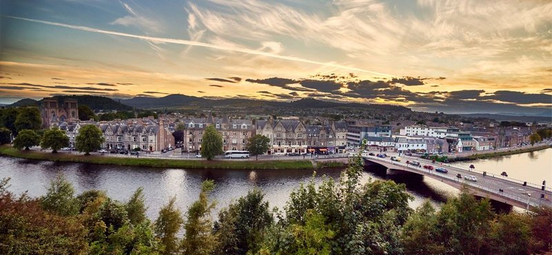 Riverside town at sunset with bridge, waterfront buildings and forested banks
