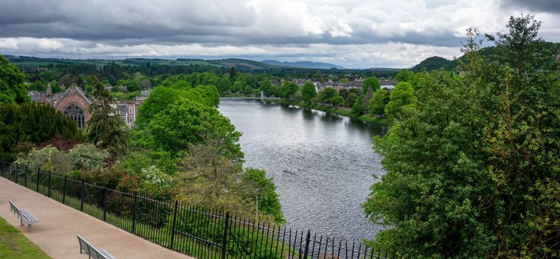 River valley landscape view with green trees, distant buildings, and cloudy sky