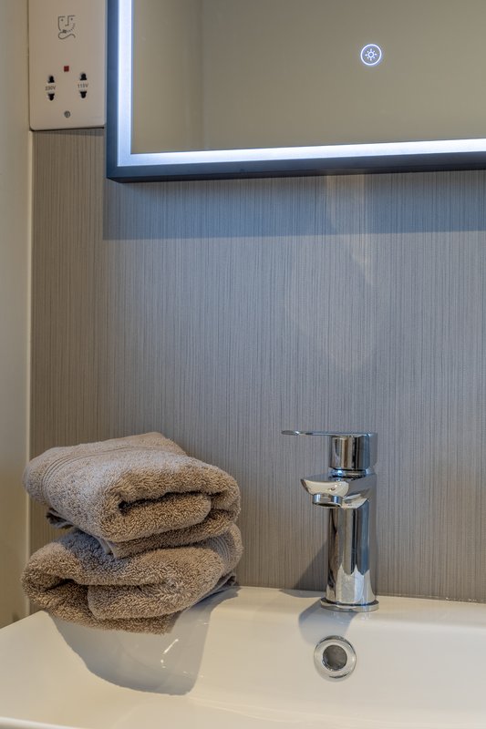 Modern bathroom sink with chrome faucet, stacked towels, and wall-mounted clock