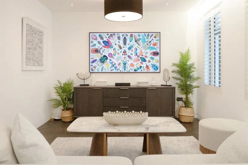 Modern living room with marble dining table, cream upholstered chairs, dark wood credenza, and framed artwork