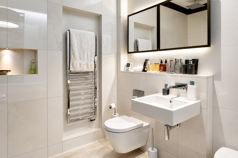 Modern bathroom with white tiles, wall-mounted sink, toilet, heated towel rail and mirror