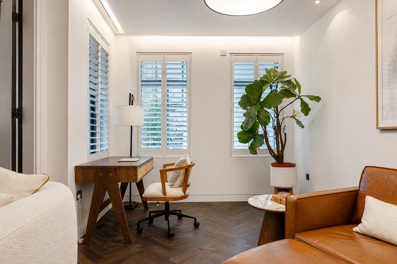 Bright bedroom with desk, wooden chairs, potted plant, and modern shuttered windows