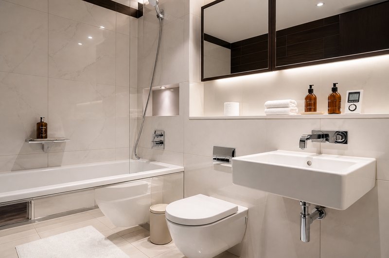 Modern bathroom with white tiles, bathtub, toilet, sink and illuminated mirror cabinet