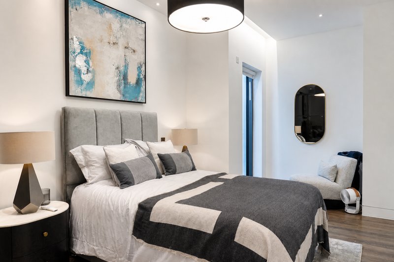 Modern bedroom with grey upholstered headboard, white bedding, black and grey throw blanket, contemporary artwork and ceiling light
