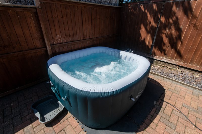Inflatable hot tub with blue water in paved outdoor courtyard with wooden fencing