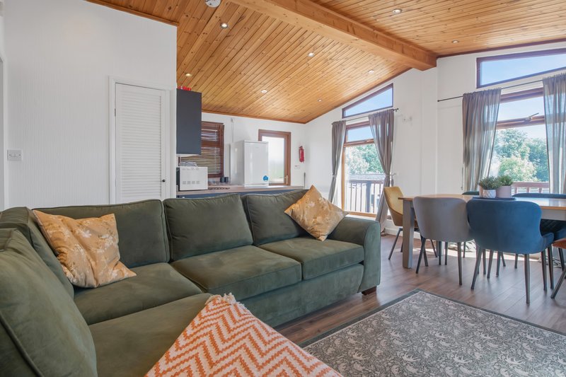 Open-plan living area with green sectional sofa, wooden ceiling, and dining area visible