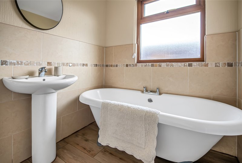 Bathroom with freestanding bathtub, pedestal sink, round mirror and window