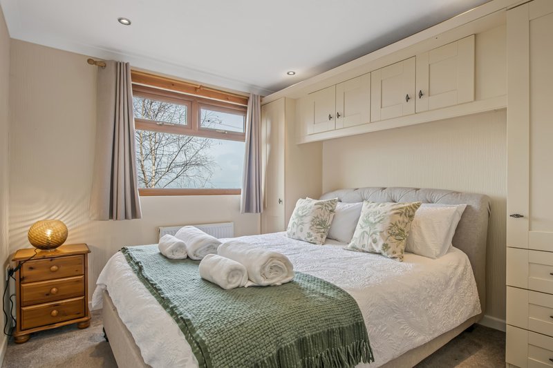 Bright bedroom with double bed, rolled towels, green throw, wooden bedside table and built-in wardrobe