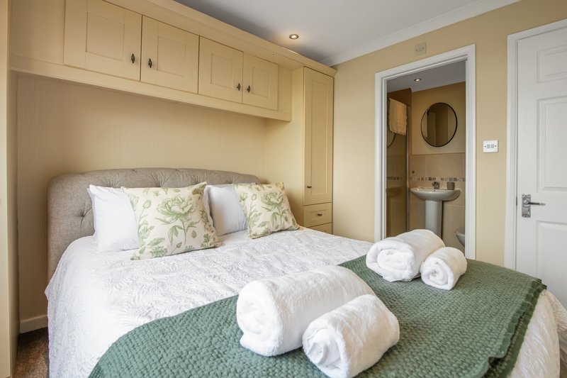 Compact bedroom with double bed, rolled towels, wooden cabinetry and ensuite bathroom visible