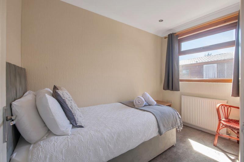 Bright bedroom with double bed, multiple pillows, blue throw blanket, and window with curtains