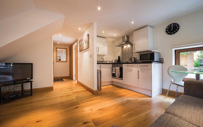 Open-plan living and kitchen area with wooden flooring, modern appliances, and natural light