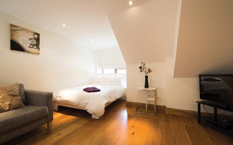 Bright attic bedroom with wooden floor, double bed, armchair and small side table