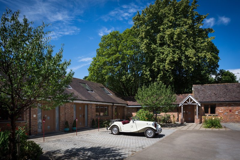 Brick property courtyard with white vintage car, paved driveway and mature trees