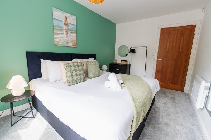 Bedroom with double bed, green accent wall, bedside lamp and wooden door