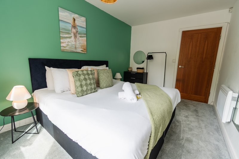 Bright bedroom with green accent wall, double bed, white pillows and green throw, bedside lamp