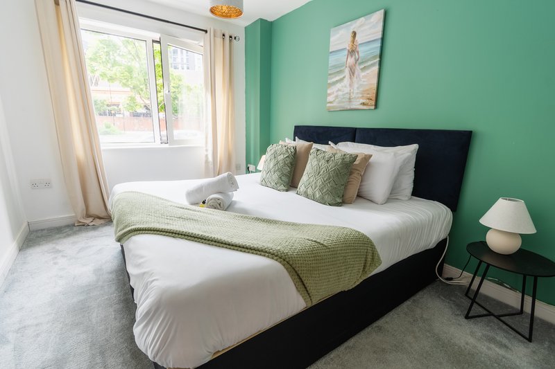 Bright bedroom with double bed, green accent wall, white bedding and decorative pillows