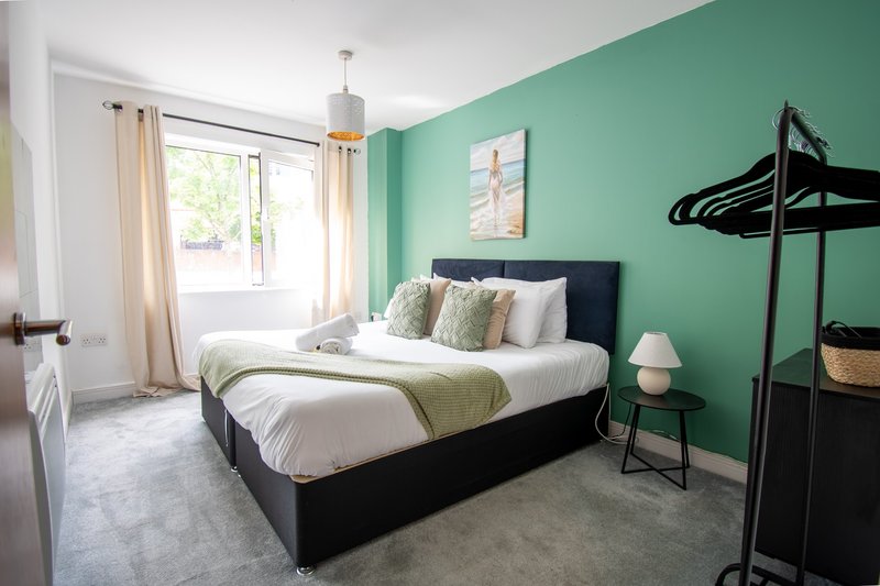 Bright bedroom with mint-green walls, black bed frame, white bedding, and garden view through window