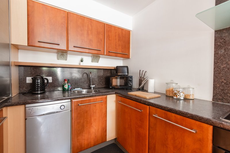 Modern kitchen with orange wood cabinetry, black countertop, stainless steel appliances and sink