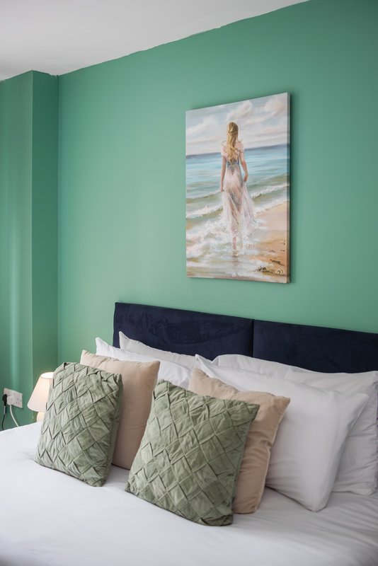 Bedroom with turquoise walls, black headboard, white bedding, and patterned green cushions