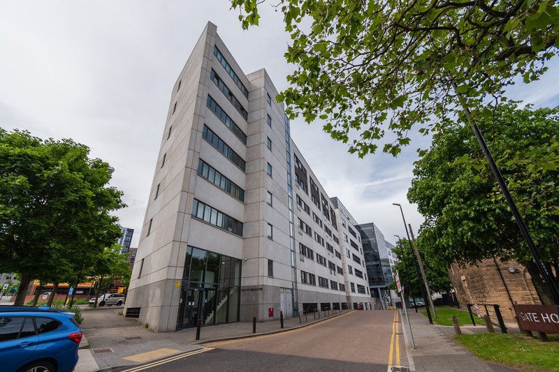 Modern multi-story residential building exterior with street view and surrounding trees