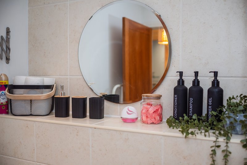 Bathroom vanity with round mirror, toiletries, black bottles, and decorative plants