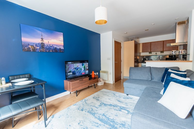 Open-plan living room with blue accent wall, sofa, TV, and kitchen area visible