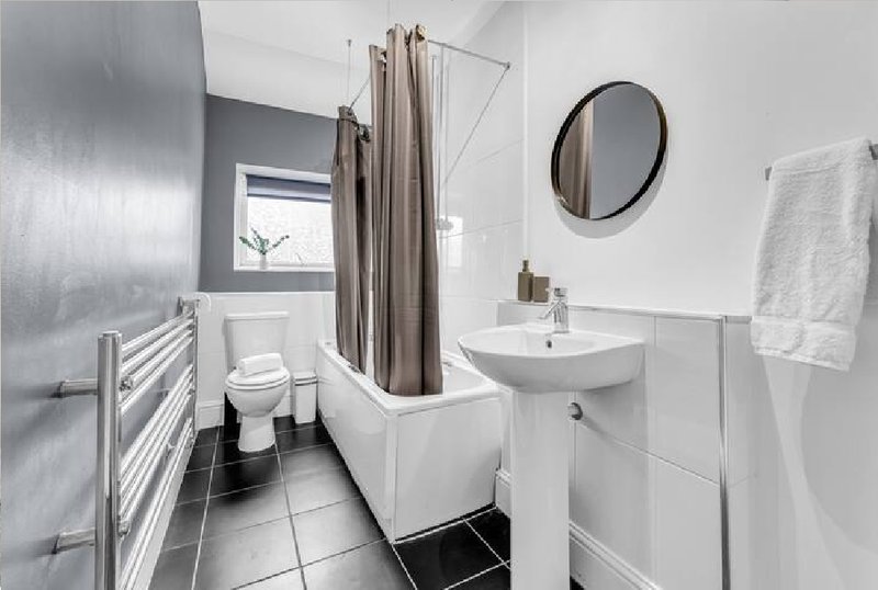 Modern bathroom with white suite, shower enclosure, heated towel rail, round mirror and black floor tiles
