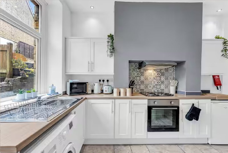 Modern kitchen with white cabinetry, integrated appliances, gray accent wall and garden view