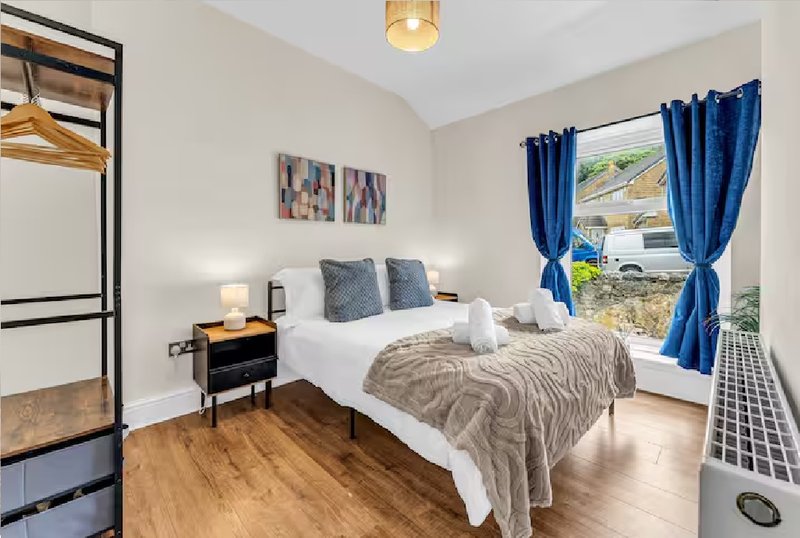 Bright bedroom with double bed, wooden floor, blue curtains and bedside table