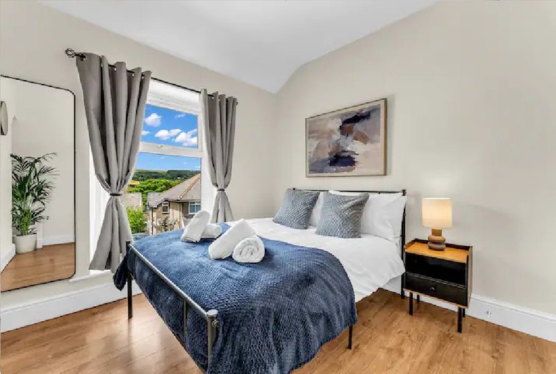 Bright bedroom with double bed, grey curtains, wooden floor and countryside view from window