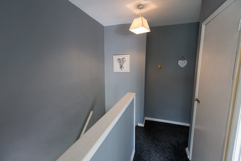 Narrow hallway with blue-gray walls, white handrail, pendant light fixture, and dark carpet flooring