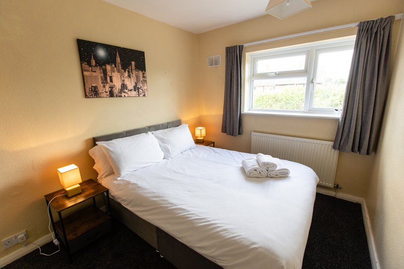 Bright bedroom with double bed, white linens, bedside lamps, and large window with gray curtains