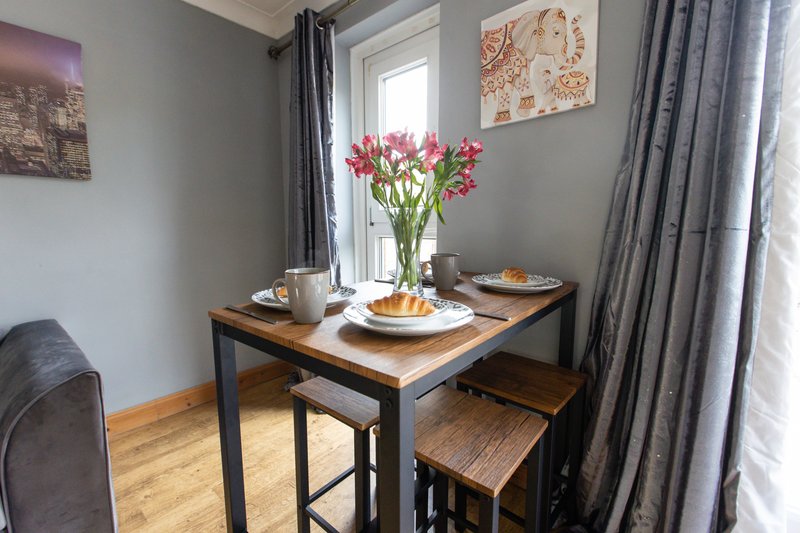 Dining table set for two with pink flowers, plates, and window view with curtains