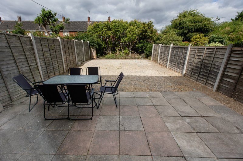 Paved garden patio with dining table, chairs, and wooden fencing surrounding the space