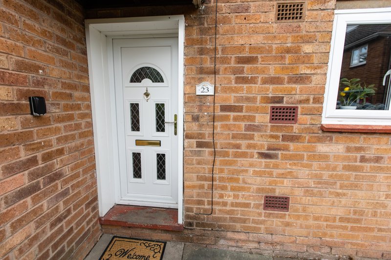 Red brick house exterior with white front door, transom window, and welcome doormat