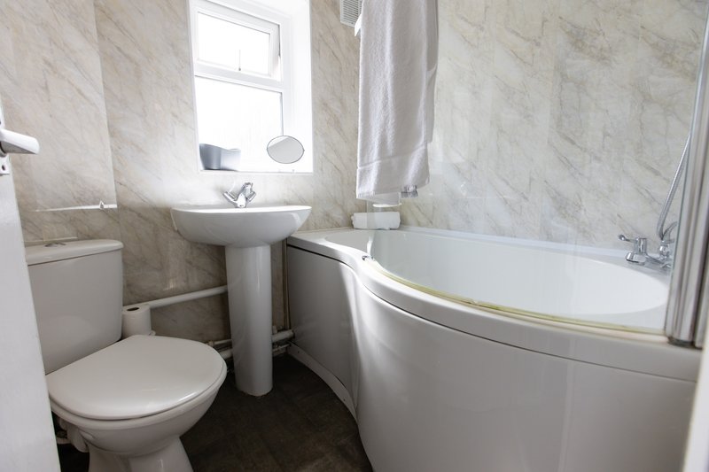Clean bathroom with toilet, pedestal sink, bathtub and small window