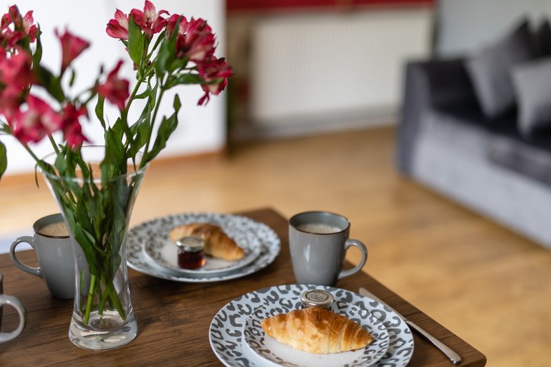 Wooden table set with plates, croissants, flowers in vase, and cups