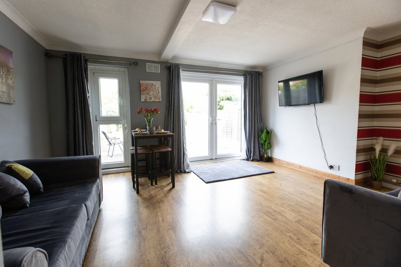 Modern living room with wooden flooring, dark sofas, wall-mounted TV and glass patio doors