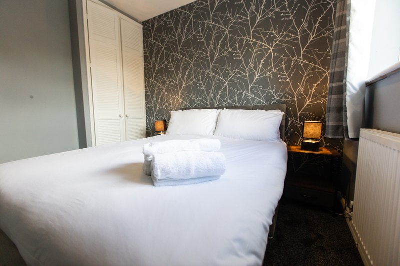 Bedroom with white double bed, patterned headboard wall, bedside lamps and wardrobe
