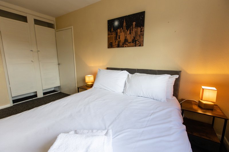 Bedroom with double bed, white bedding, two bedside lamps and cityscape wall art